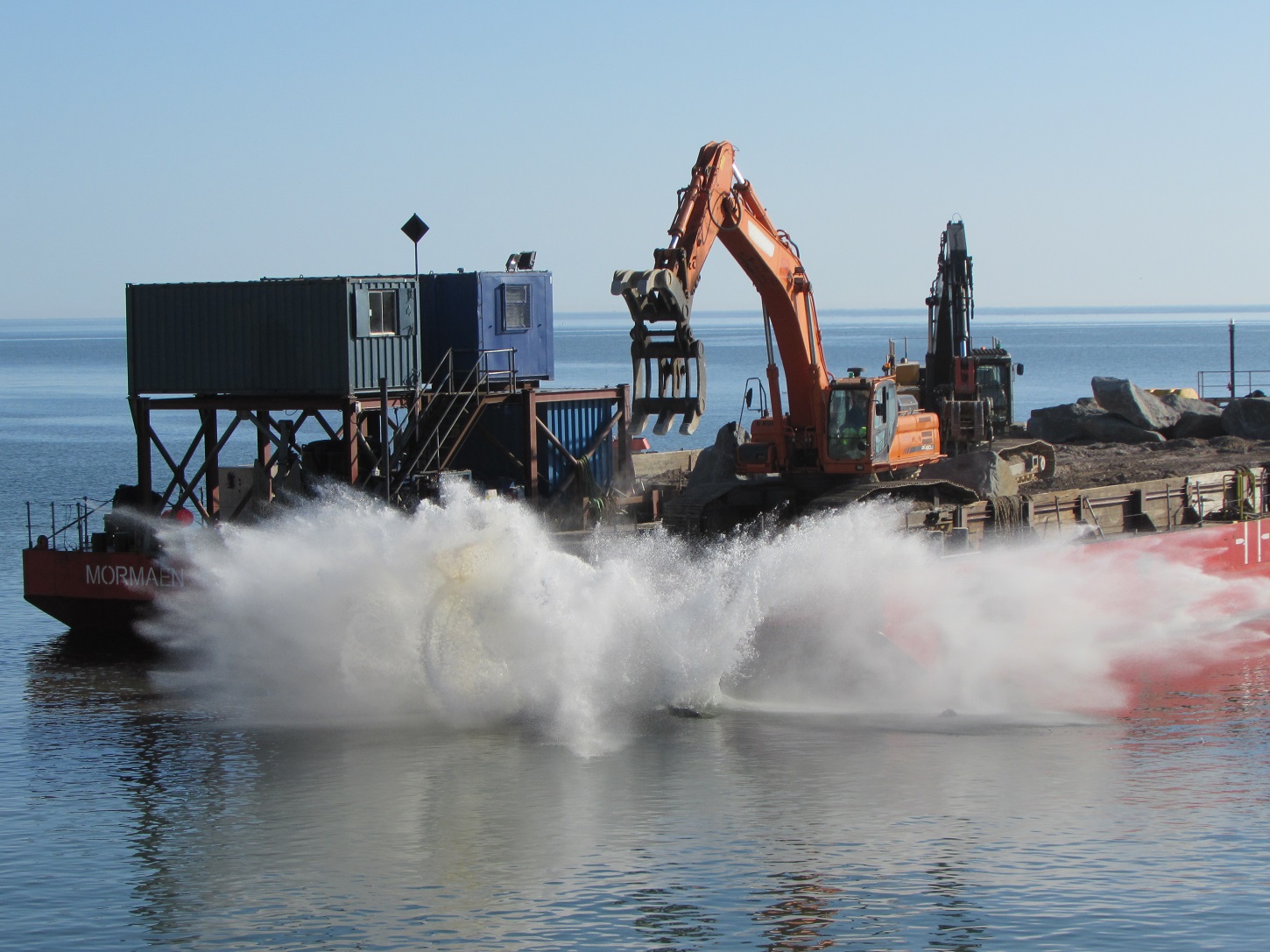 Runswick Bay Coastal Protection - image shows barge with boulders being pushed by digger into the sea, to form the coastal defences